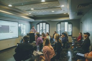 Professor teaching a full lecture hall in front of a large projection screen
