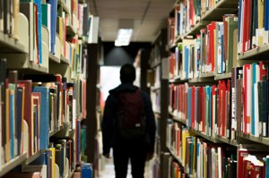 A student walking down a long, bright library aisle