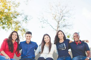 Five students sitting together outdoors on campus, smiling